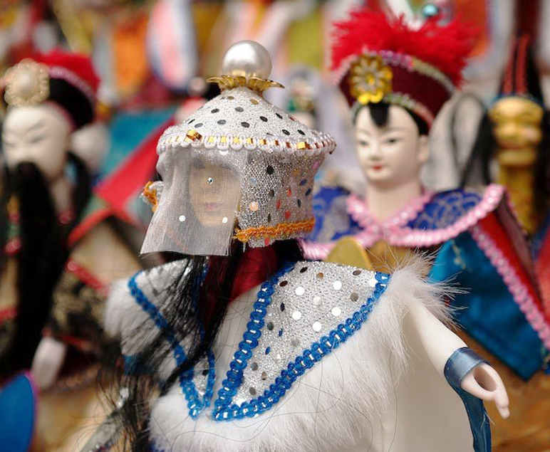 화려한 전통 의상을 입은 인형들, 모자와 베일을 쓴 인형이 전면에 보이고 뒤쪽에 다른 인형들이 놓여 있는 모습