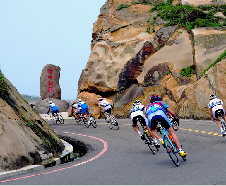 굽이진 해안 도로에서 여러 명의 자전거 선수들이 바위 절벽 사이를 달리고 있는 모습