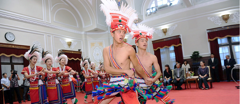 전통 의상을 입은 남녀가 깃털 장식 모자를 쓰고 실내에서 춤을 추는 모습